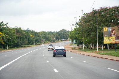 Photo de un large avenue à Yamoussoukro, le political capital de Côte d'Ivoire, lined avec tropical trees et advertising billboards.