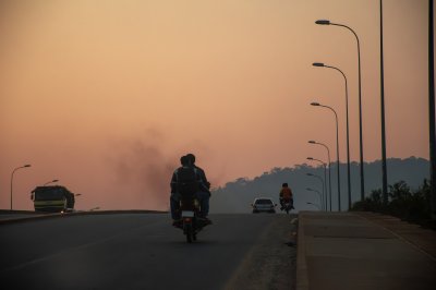 Un road scene à Yaoundé, Cameroun, à coucher de soleil. sous un vibrant orange ciel, motorcyclists et vehicles move forward à silhouette, embodying urban life à crépuscule.