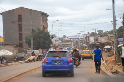 Realistic photograph de un rue à Yaoundé, le capital de Cameroun. It shows vehicles, yellow taxis, moto taxis, et pedestrians à un animé urban setting.