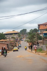 Realistic photograph de un neighborhood rue à Yaoundé, le capital de Cameroun. le image shows residents marchant, moto taxis, et cars roulant entre coloré houses.