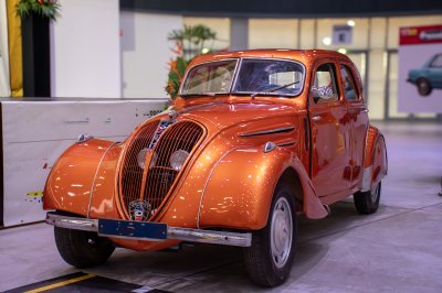 Un vintage Peugeot 402, restauré et displayed à un moderne space. Its lumineux copper-orange color