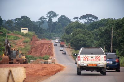 Un red laterite road lined avec vegetation, typical de rural camerounais landscapes, connecting villages et forests.