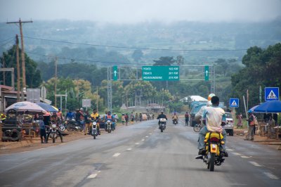 Un moto taxi driver crosses un road lined avec houses et palmiers, un typical image de everyday life à Cameroun.