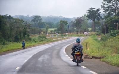 Un motocycliste rides along un tree-lined road à le camerounais countryside, illustrating local mobility et rural tranquility.
