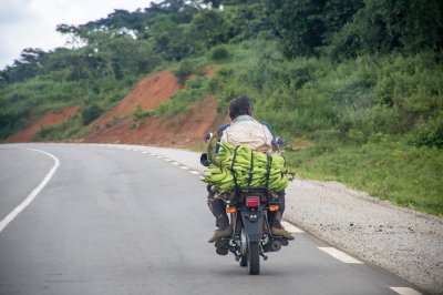 Motocycliste traveling sur un paved road à rural Africa, carrying marchandises