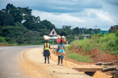Documentary photograph showing women marchant along un rural road, carrying loads sur their heads, à un tropical africain landscape.