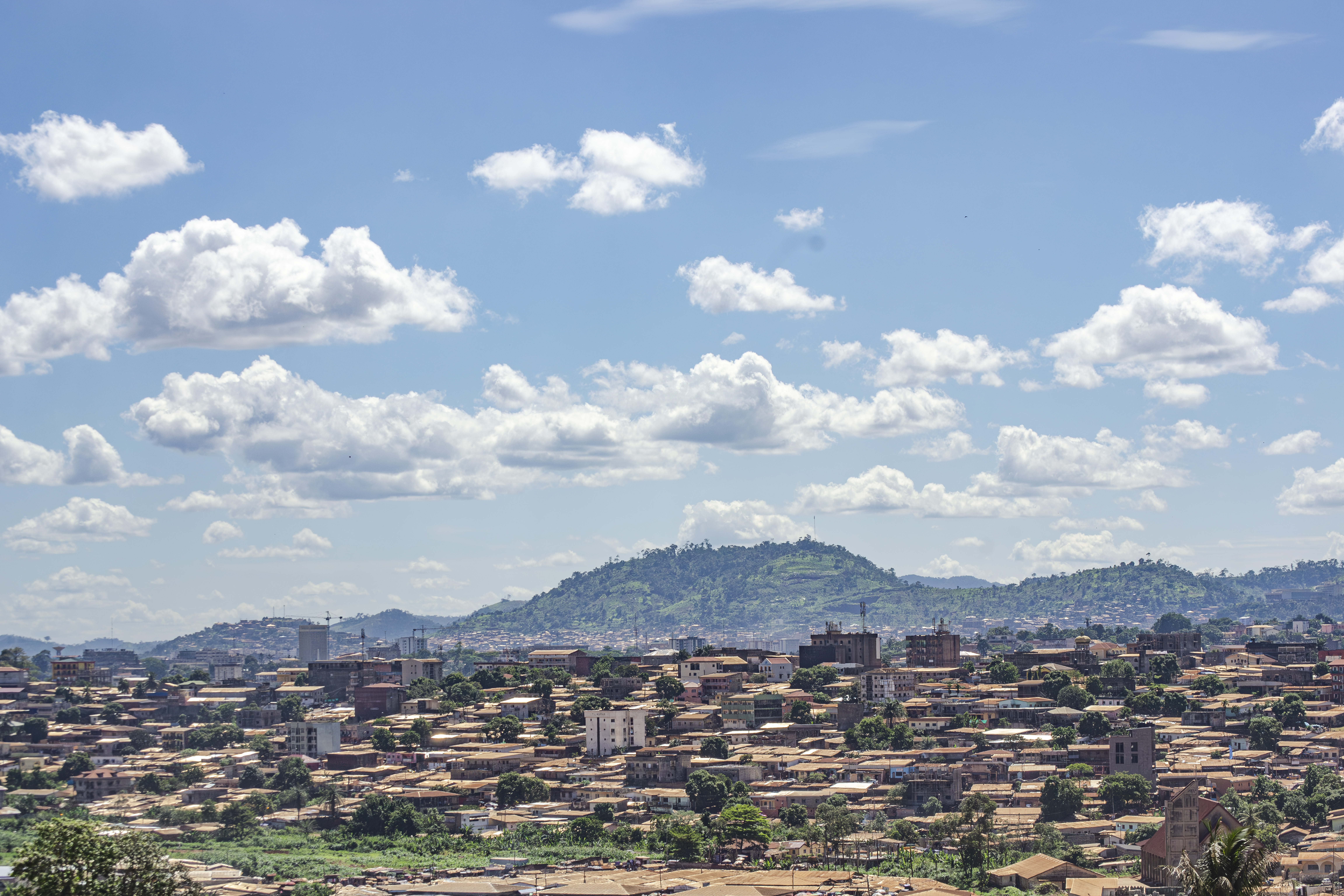 Vue aérienne panoramique de le city de yaounde à Cameroun, avec un chaîne de montagnes à le background, et un ciel bleu avec nuages.