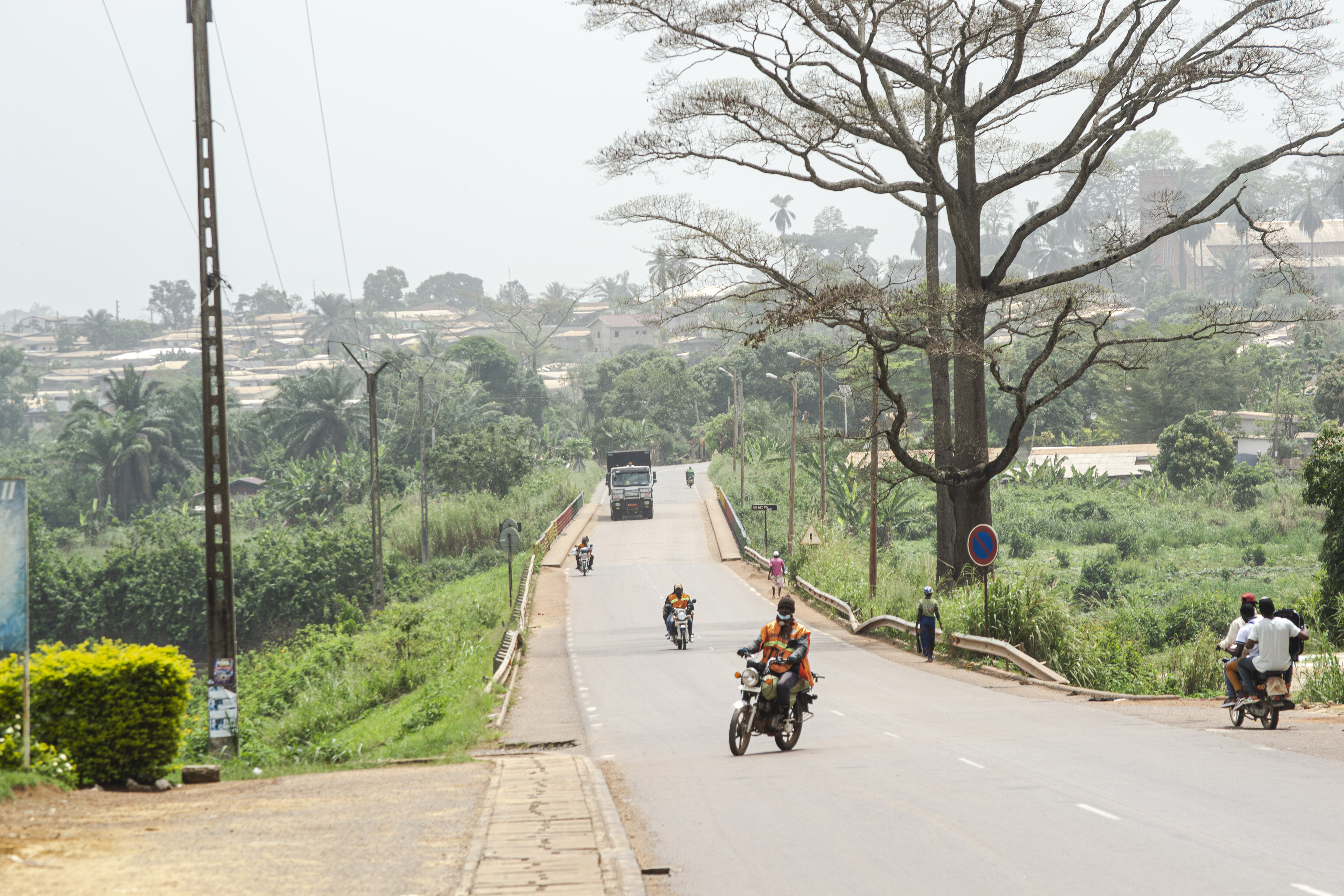 Moto traversant un rue à le oyack quartier de mbalmayo avec le new pont, verdure et grands arbres à le background